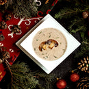 Mushroom soup in a white bowl surrounded by Christmas decorations on a dark surface