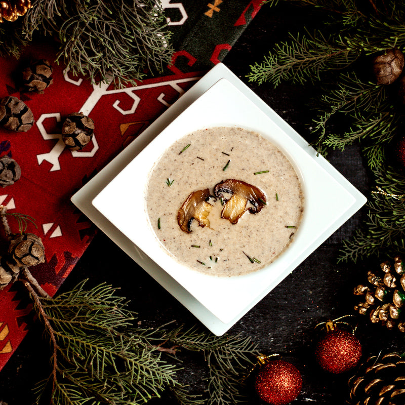 Mushroom soup in a white bowl surrounded by Christmas decorations on a dark surface