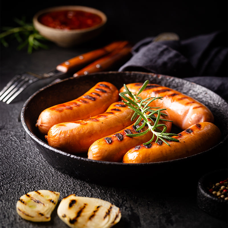Grilled sausages with rosemary in a black pan on a dark surface
