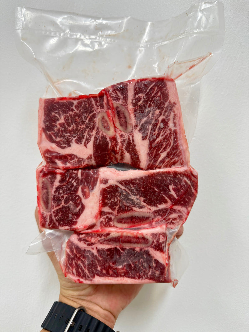 Three pieces of raw beef held in a hand against a white background