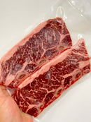 Close-up of a piece of marbled red meat held by a hand on a white background