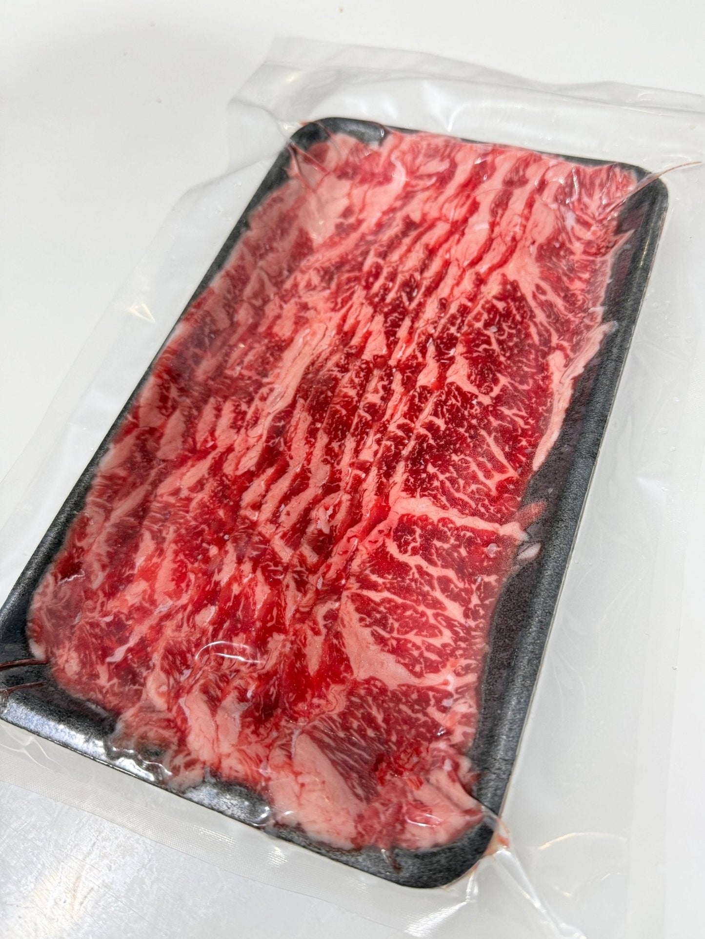 Marbled red meat on a black tray with a white background