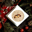 Mushroom soup in a white bowl surrounded by Christmas decorations on a dark surface