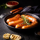 Grilled sausages with rosemary in a black pan on a dark surface