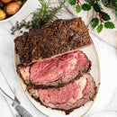 Roast beef with a slice cut on a decorative plate with herbs, on a white tablecloth.